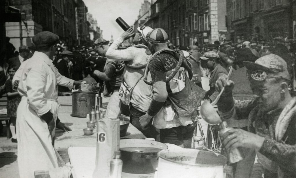 Omschrijving: Wielrennen. Tour de France/Ronde van Frankrijk 1926, 1e etappe Evian- Mulhouse (373 km), Frankrijk 20 juni 1926. Foto: Het peloton tijdens de ravitaillering in Pontarlier, de renners lessen hun dorst en vullen de bidons.